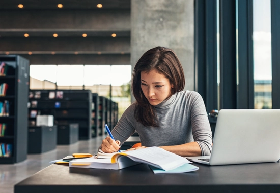 young women studying with laptop and books in library.
