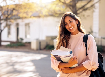 Young woman holding books outdoors on campus.