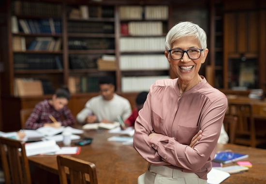 a woman crossing her arms and smiling, there are students in the background working