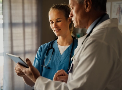 Two healthcare workers reviewing tablet data.