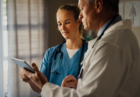 Two healthcare workers reviewing tablet data.