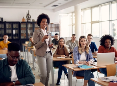A classroom with students and a teacher standing in the middle clicking a remote