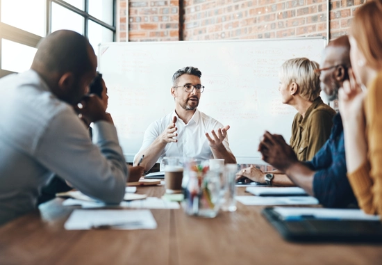 Group discussion around a table with whiteboard in background.