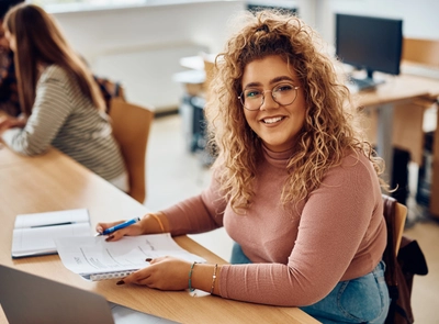Woman reviewing papers at desk in classroom with other students.