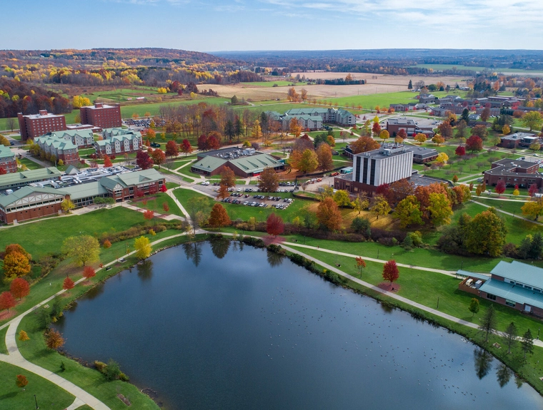 a very large college campus with a pond in the middle and red trees