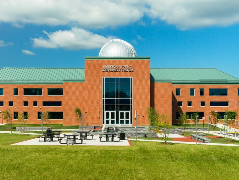 brick campus building with a green roof, picnic tables, trees, and grass in the front