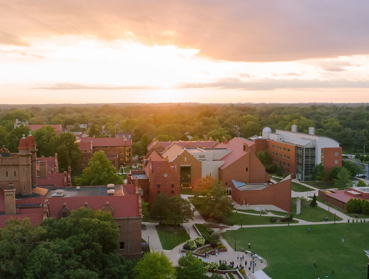 brick campus buildings spread out with a lot of trees and the sun is setting