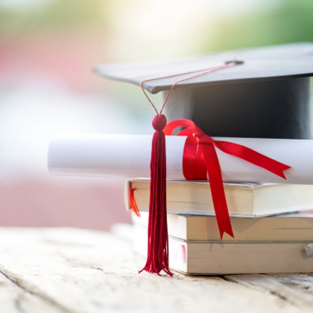 Graduation cap sitting on top of a diploma and three books on a table
