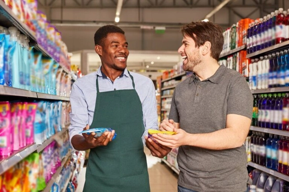 Two men in a grocery store. One is an employee and he's wearing an apron.