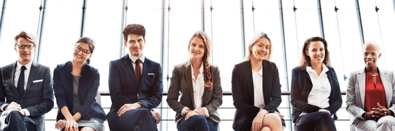 A group of people dressed in business clothes. They are sitting down and smiling.