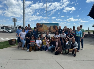 An image of many people posing around a state sign for South Dakota.